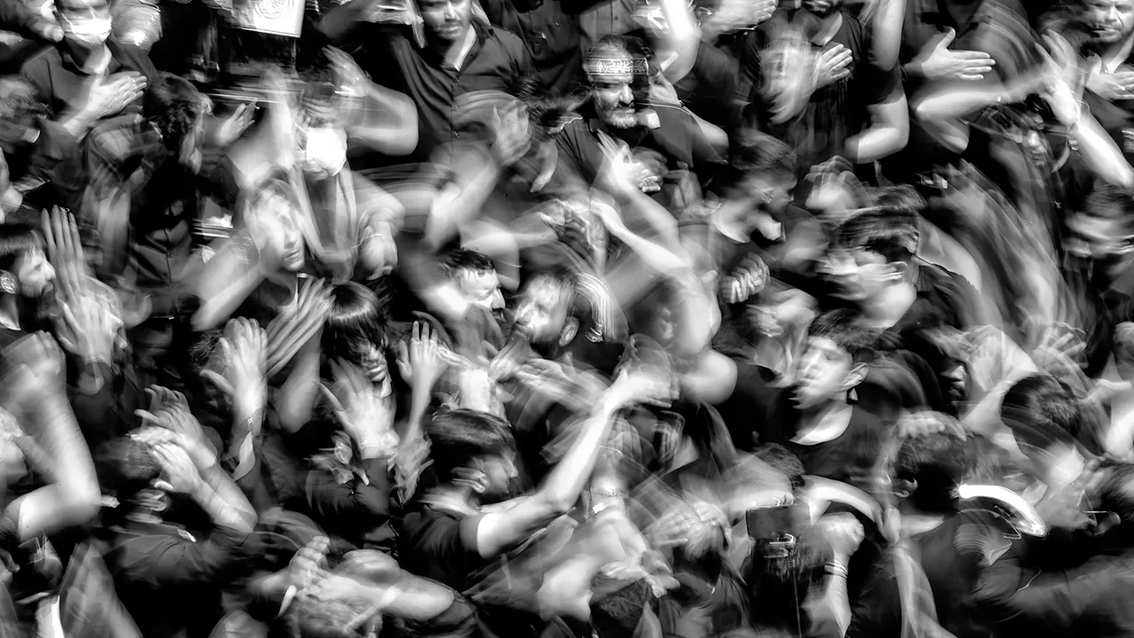 A packed crowd from above in black and white, hands raised and blurred with movement.