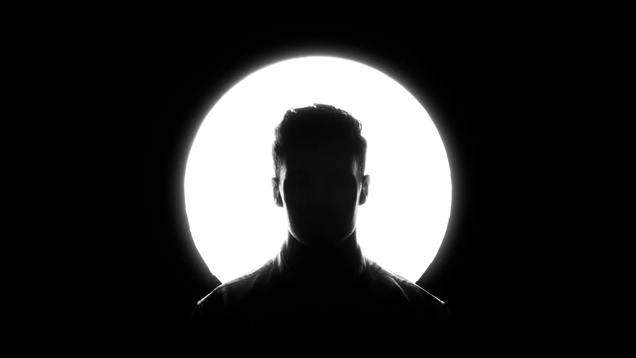A head and shoulders in silhouette against a white disc of light.