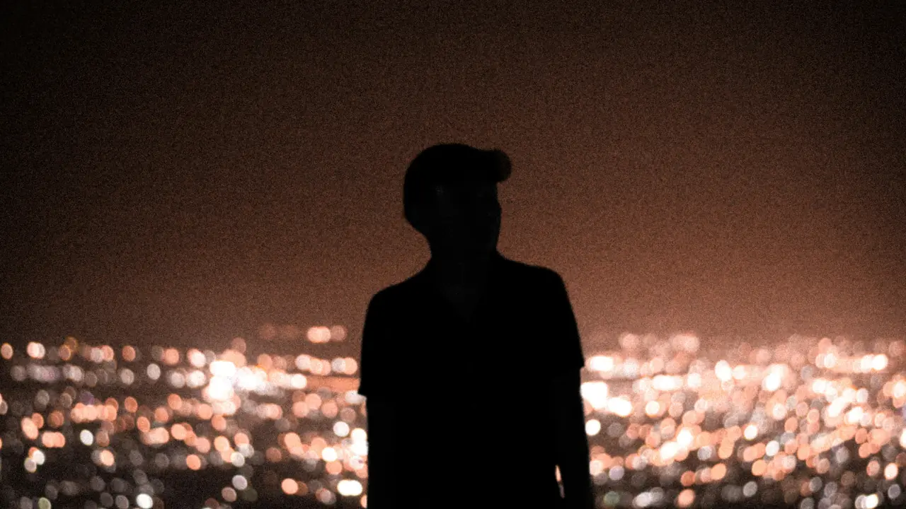 A figure in silhouette above a city’s lights at night.