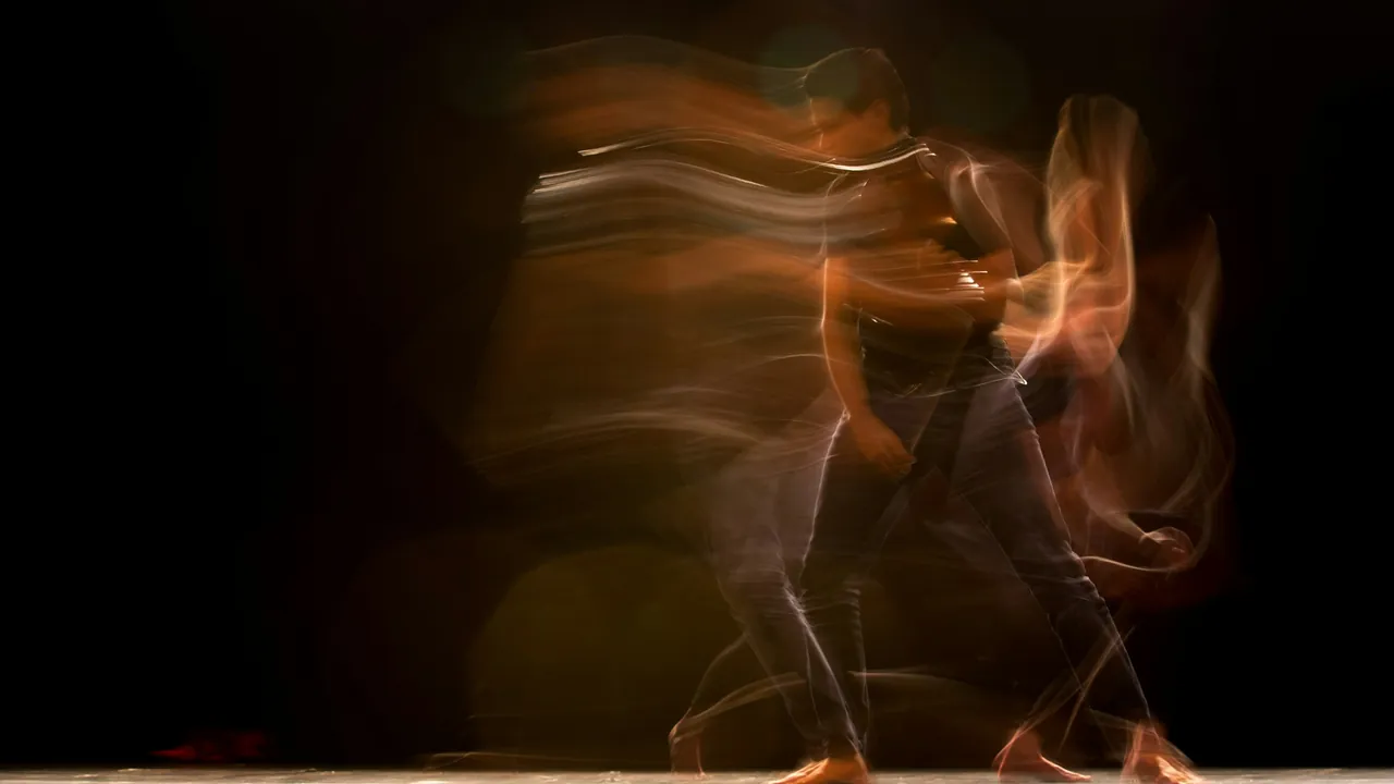 A dancer traced in warm streaks of light by a long exposure.